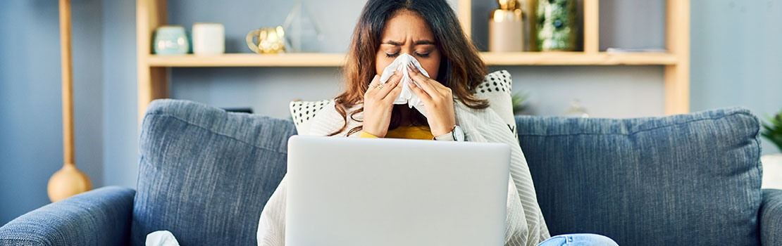 Woman with cold sitting on sofa with laptop in front of her