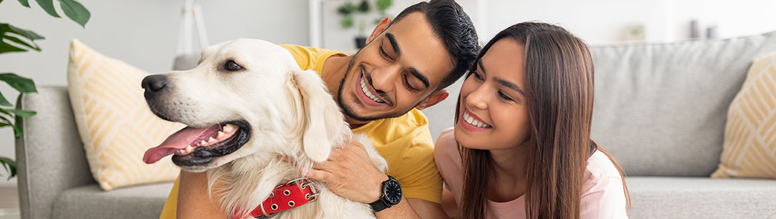 Happy couple at home sit on the floor and cuddle their dog.